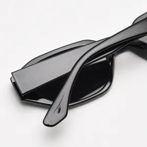 Gros plan de lunettes de soleil polygonales noires étroites aux branches brillantes et élégantes.