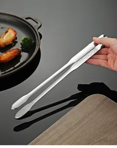 Close-up view of stainless steel barbecue tongs with hammered handle, showcased in a kitchen dining scene.