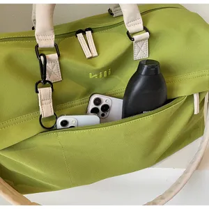 Detail view of large capacity green travel duffel bag with beige handles and front pocket.