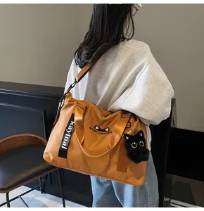 Détail de sac de voyage montrant un intérieur spacieux, une sangle robuste et un pendentif chat.