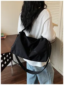 Vue détaillée d'un sac de voyage noir en toile avec large sangle et poche zippée.