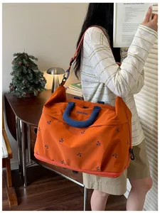 Gedetailleerd overzicht van grote oranje reistas met blauwe handvatten en strik borduursel.