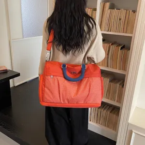 Detailed view of the large travel duffel bag worn on shoulder, showing orange grid fabric.