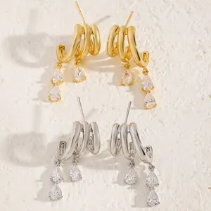 Macro view of gold and silver layered C-hoop earrings with dangling pear-shaped crystals.