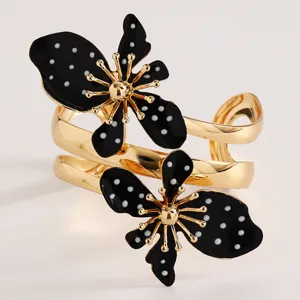 Detailansicht eines goldenen Armreifs mit schwarzen gepunkteten Retro-Blumenmotiven
