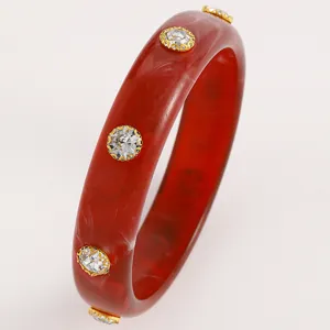 Close-up of retro red acrylic bangle with embedded crystal studs in gold settings