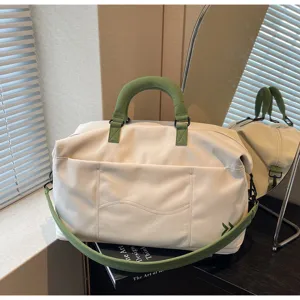 Detail view of large capacity travel duffel bag in off-white with green handles and strap.