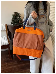 Vista dettagliata della grande borsa da viaggio, motivo scozzese arancione e marrone con manici.