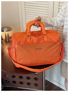 Détail de sac de voyage orange, grand sac week-end en nylon avec poche avant pratique.