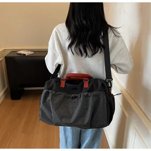 Detail view of large capacity travel duffel bag with plaid front pocket and red handle.