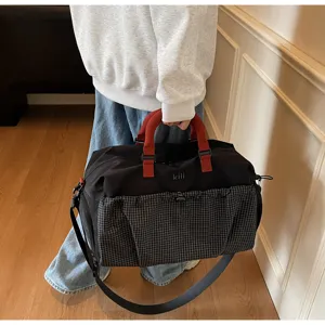 Close-up detail of the black travel duffel bag with red handles and front grid pocket.