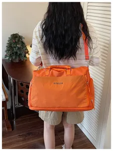 Détail du grand sac de voyage orange, montrant la bandoulière et la poche avant zippée.