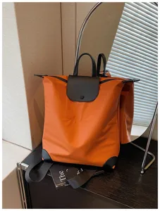 Vista dettagliata del pratico zaino arancione da viaggio con patta in pelle nera e nylon resistente.