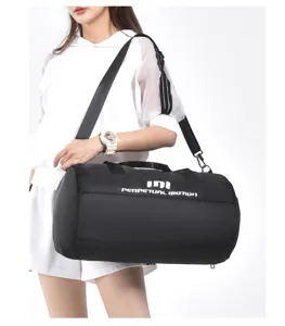 Detail shot of black cylindrical gym duffel bag with shoulder strap being worn by model.
