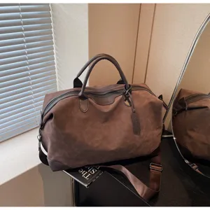Dettaglio della borsa da viaggio marrone con morbida texture in camoscio, manici e tracolla.