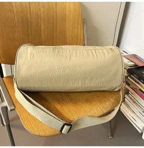 Beige cylindrical crossbody bag, casual sports duffel and travel shoulder bag for daily use.