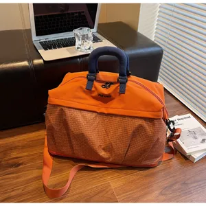 Vista detallada de la gran bolsa de viaje con asas azules y patrón de cuadrícula naranja.
