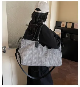 Dettaglio della grande borsa da viaggio con motivo a spina di pesce e manici neri resistenti.
