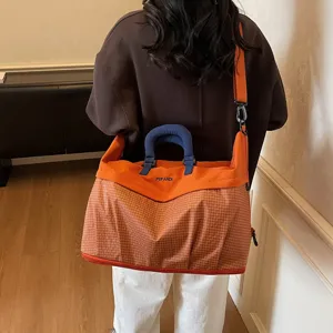 Vista detallada de la gran bolsa de viaje naranja a cuadros con asa azul y correa de hombro.