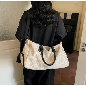 Dettaglio di una borsa da viaggio capiente con manici in pelle nera e tessuto canvas.