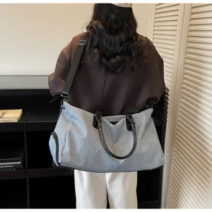 Vista dettagliata di una borsa da viaggio capiente con elegante motivo a spina di pesce e manici.