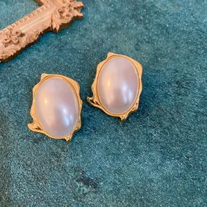 Close-up detail of retro court-style oval pearl earrings with gold irregular trim for women.