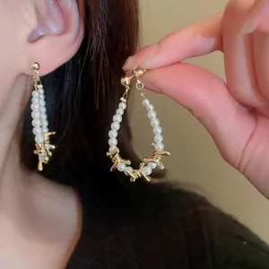 Close-up view of elegant pearl drop earrings with golden twisted metal details, worn on ear.