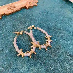 Close-up detail shot of gothic punk style barbed wire pearl hoop earrings in gold finish.