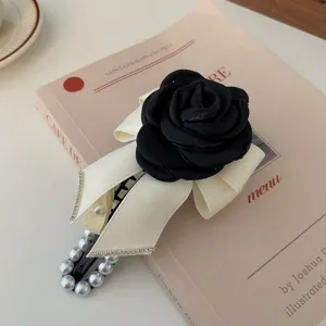 Elegante schwarze Kamelienblüten Haarklammer mit cremefarbener Schleife und Perlen.