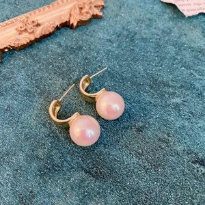 Close up of vintage style C-shaped gold metal and pink pearl stud earrings detail shot