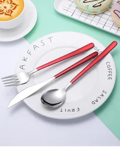 Edelstahl Besteck Set Detailansicht mit rotem Griff Messer Gabel und Löffel auf Teller.