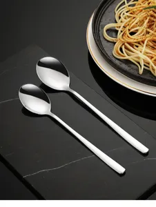 Detailansicht von langen Edelstahl-Suppenlöffeln auf dunklem Marmortisch mit Pastagericht.