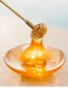 Close-up detail of golden stainless steel spiral stirring rod lifting thick honey texture.