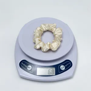 Detailed shot of a sleek beige satin hair scrunchie shown on a digital scale weighing 6.8g.