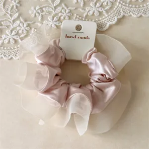 Detailaufnahme eines rosa Satin- und Organza-Haargummis mit Etikett, elegante Textur.