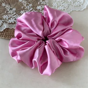 Close-up of a large pink satin scrunchie detail, soft glossy fabric for gentle hair styling.