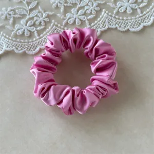Pink satin hair scrunchie detail close-up, smooth fabric texture and elastic band for hair.