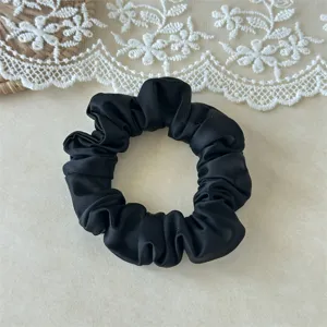 Close-up of a sleek black satin hair scrunchie on a lace background, soft touch, simple style.