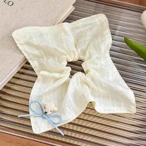 Close-up detail of cream white scrunchie with cute blue bow and mini bear charm for sweet hairstyles.