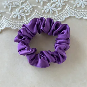 Close up view of purple satin scrunchie detail, smooth fabric hair tie surface texture.