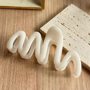 Close-up detail shot of a stylish milk-white wavy hair claw clip on wooden background.