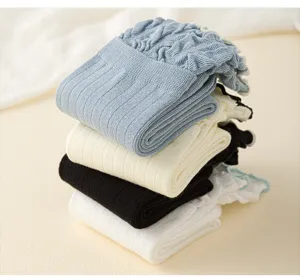 Detailaufnahme von gestapelten Baumwollsocken mit Rüschenbündchen in Blau, Weiß und Schwarz.