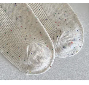 Close-up detail of cream speckled knit socks featuring ribbed texture and colorful dots.