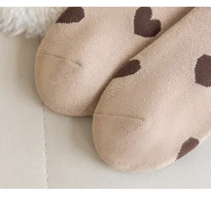 Gros plan de chaussettes d'hiver douillettes beiges avec motifs de cœurs marron.