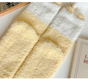 Nahaufnahme von flauschigen gelb-weißen Korallenfleece-Süßsocken mit niedlichen Katzenohren.
