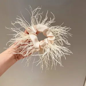 Close-up of beige satin scrunchie adorned with fluffy white ostrich feathers, elegant detail.