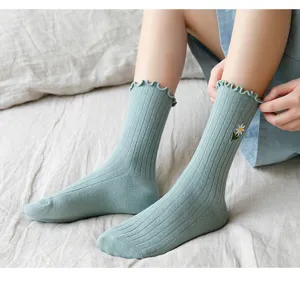 Detailansicht von gerüschten grünen Socken mit süßer Gänseblümchen-Bestickung im Bett.