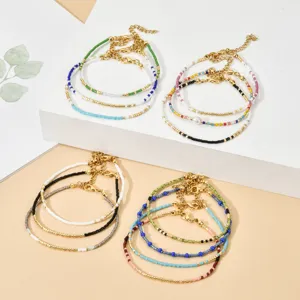 Gros plan détaillé de bracelets empilables en perles de rocailles et chaînes dorées.
