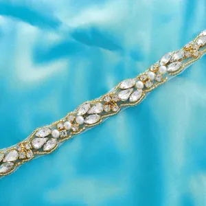Detailed shot of sparkling rhinestone belt applique with clear crystals and pearls on blue satin.