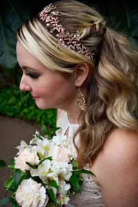 Detailed shot of a bridal rose gold rhinestone and pearl headband worn by a model in a wedding setting.